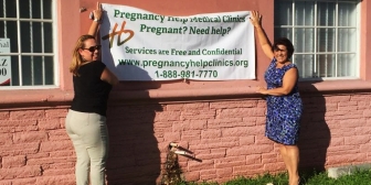Jeanne Pernia (left) and Martha Avila hang their sign on the wall of an ex-abortion facility that is now home of Heartbeat of Miami&#039;s fourth location.
